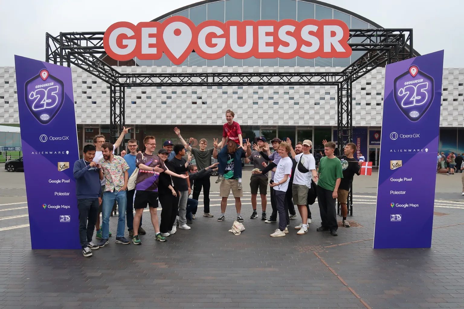 Danske GeoGuessr-spillere jubler foran indgangen til GeoGuessr-VM 2025 i København. En af dem sidder på en andens skuldre.